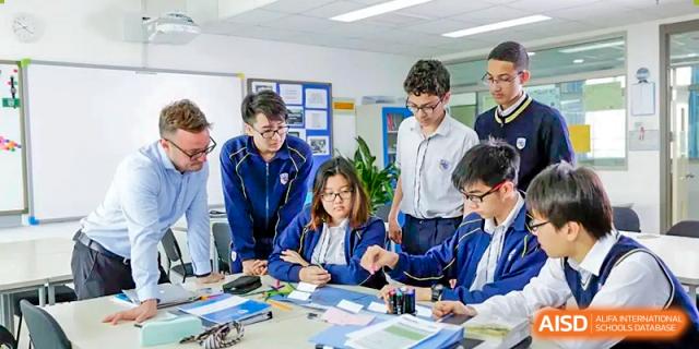 A diverse group of students and a teacher collaborating intently around a table covered in documents during a team project at BIBA (Tianjin International Bilingual Academy).