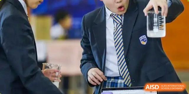 Detail of a student in a blue and yellow striped school tie and uniform looking down at a digital tablet or device at BIBA (Tianjin International Bilingual Academy).