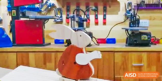 A close-up of a student-built wooden robot or animal model on a workbench, with tools and materials in the background at BIBA (Tianjin International Bilingual Academy).