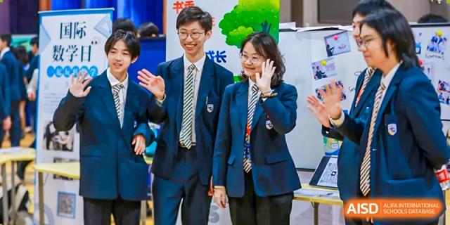 Two high school students in navy and green school uniforms smiling and waving in an exhibition or common area at BIBA (Tianjin International Bilingual Academy).