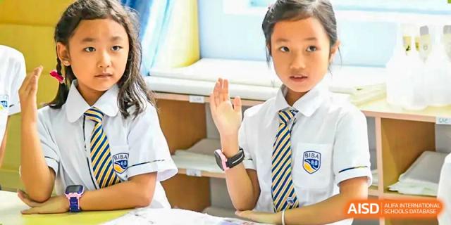 A young male student in a white shirt and school tie actively raising his hand to answer a question in class at BIBA (Tianjin International Bilingual Academy).