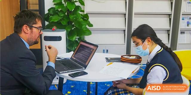 Two students working together at a round white table with a laptop open and notes spread out in a study area at BIBA (Tianjin International Bilingual Academy).