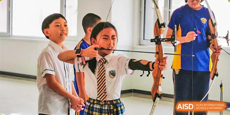 Female student in a school uniform practicing archery indoors, aiming a bow and arrow with instruction at BIBA (Tianjin International Bilingual Academy).