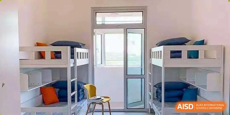 Dormitory room with bunk beds and a large window or glass door letting in light, showing student living accommodations at BIBA (Tianjin International Bilingual Academy).