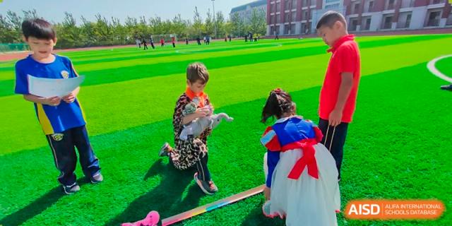 Young children in costume walking on a vibrant green sports field on a sunny day at BIBA (Tianjin International Bilingual Academy).