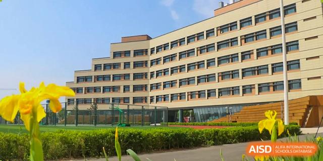 Exterior view of a modern, multi-story school building with yellow walls and rows of windows, surrounded by green landscaping at BIBA (Tianjin International Bilingual Academy).