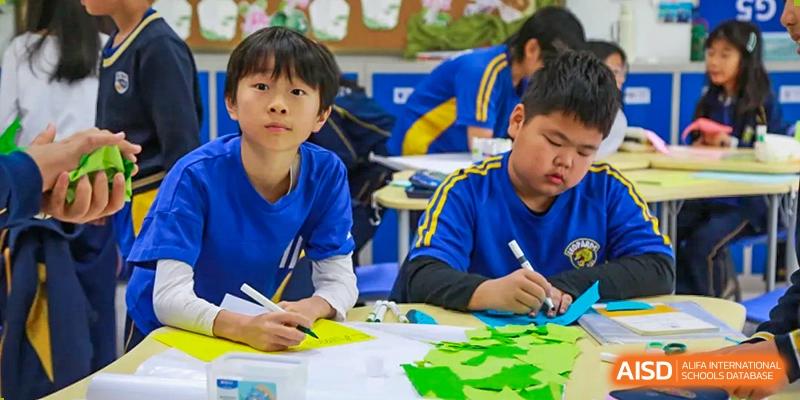Two young male students in blue uniforms working on a hands-on art or craft project at a table in a classroom at BIBA (Tianjin International Bilingual Academy).