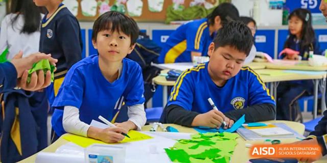 Two young male students in blue uniforms working on a hands-on art or craft project at a table in a classroom at BIBA (Tianjin International Bilingual Academy).