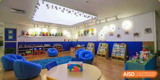 Bright, open-plan classroom or reading area with blue carpet, white walls, bookshelves, and beanbag chairs, showing an indoor learning space at BIBA (Tianjin International Bilingual Academy).