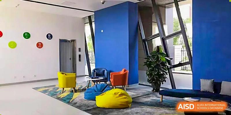 Modern lounge or common area with bright blue walls, yellow beanbag chairs, a small table, and a potted plant, showing an interior space at BIBA (Tianjin International Bilingual Academy).