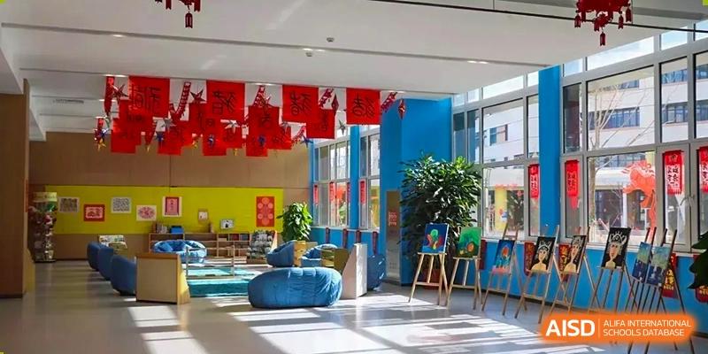 Indoor common area or lobby decorated with a blue wall, bright red hanging flags, and blue lounge seating at BIBA (Tianjin International Bilingual Academy).