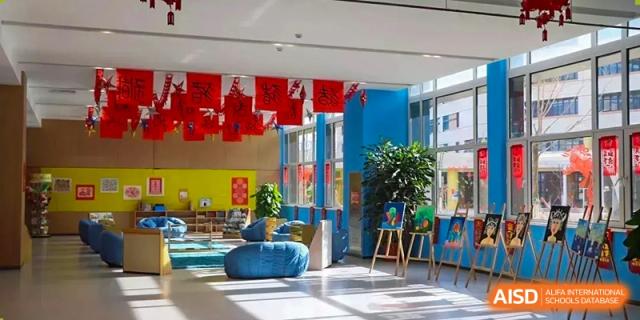 Indoor common area or lobby decorated with a blue wall, bright red hanging flags, and blue lounge seating at BIBA (Tianjin International Bilingual Academy).