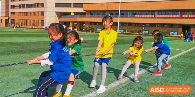 Group of young students on a sports field participating in a Tug-of-War game, demonstrating a team activity at BIBA (Tianjin International Bilingual Academy).