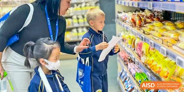A young male student in a school uniform reading a paper or list while shopping for snacks in the school canteen or store at BIBA (Tianjin International Bilingual Academy).