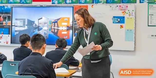 A female teacher from Dingwen Academy Hangzhou leaning over to help a student with paperwork during a lesson.