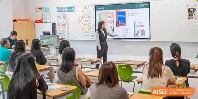 A female teacher from Dingwen Academy Hangzhou using a touchscreen board to teach students in a brightly lit classroom.