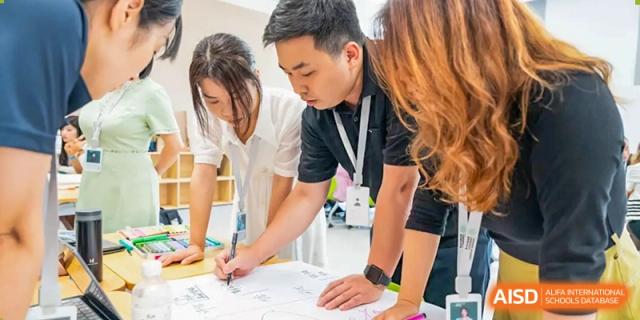 A teacher from Dingwen Academy Hangzhou leaning over a table to discuss technical blueprints or designs with a group of students.