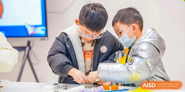 Two young male students from Dingwen Academy Hangzhou intently working together on a small technical or crafting project.