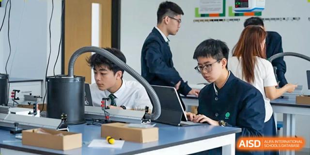 Two male students from Dingwen Academy Hangzhou working on laptops and technical equipment in a focused setting.