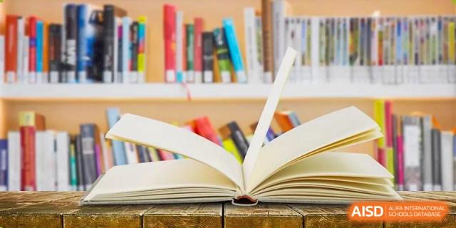 A close-up image of an open book lying on a table in the library of Dingwen Academy Hangzhou, with colorful bookshelves blurred in the background.