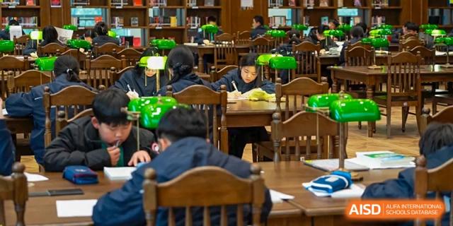 Students from Dingwen Academy Hangzhou sitting at wooden desks and reading in a traditional school library setting.
