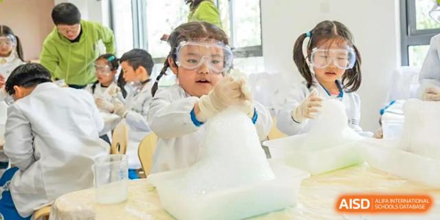 A young student from Dingwen Academy Hangzhou wearing safety goggles and gloves, performing a foaming science experiment in a lab.