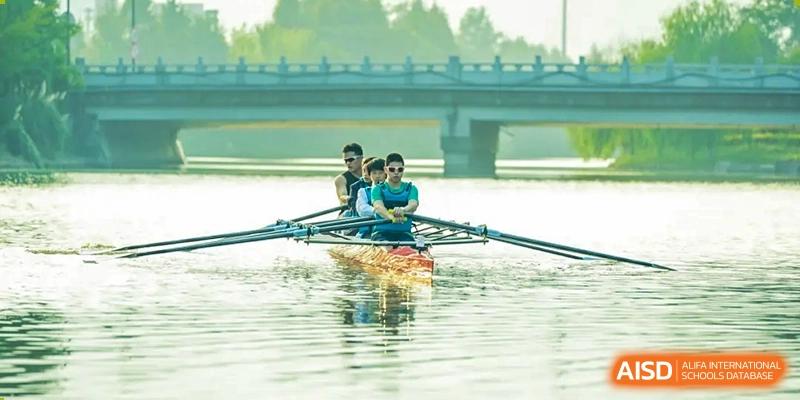 Students from Dingwen Academy Hangzhou rowing a sculling boat on the water beneath a bridge during a practice session.