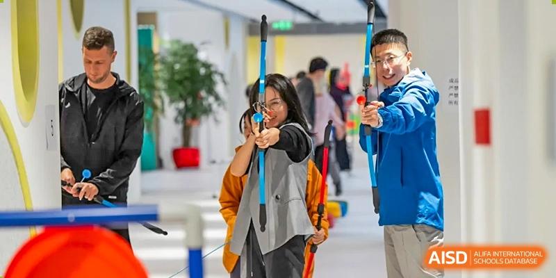 Two students from Dingwen Academy Hangzhou practicing archery indoors, aiming with bows and arrows.