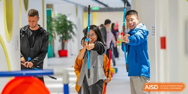Two students from Dingwen Academy Hangzhou practicing archery indoors, aiming with bows and arrows.