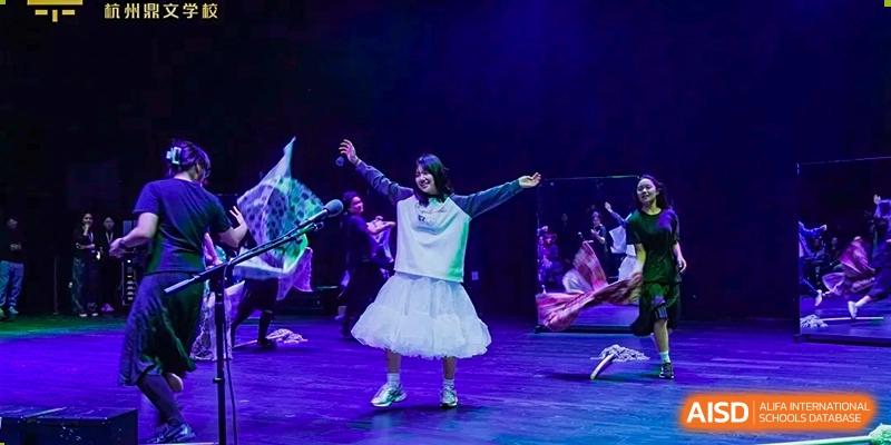 A student from Dingwen Academy Hangzhou performing a dance or theatrical piece on a dark stage in a white costume.