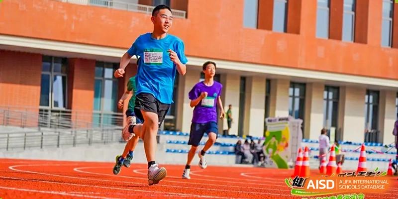 Two students from Dingwen Academy Hangzhou running together on a track past the red brick school building.
