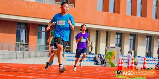 Two students from Dingwen Academy Hangzhou running together on a track past the red brick school building.