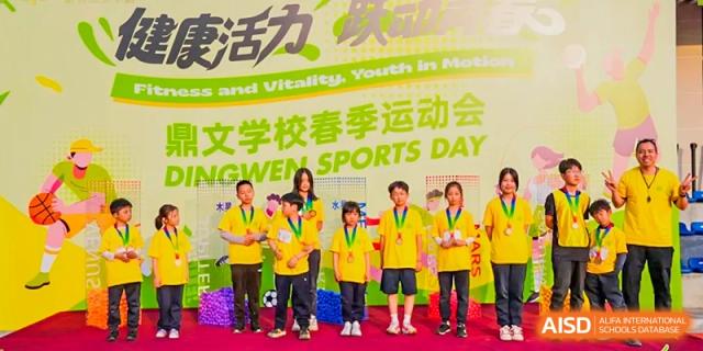 A group of students from Dingwen Academy Hangzhou posing with their gold medals on a podium during a school Sports Day event.