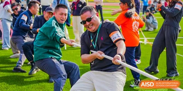 An adult from Dingwen Academy Hangzhou pulling a rope with effort during a game of tug-of-war.