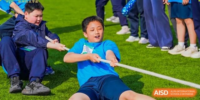 A young boy from Dingwen Academy Hangzhou in a blue shirt straining while participating in a game of tug-of-war.