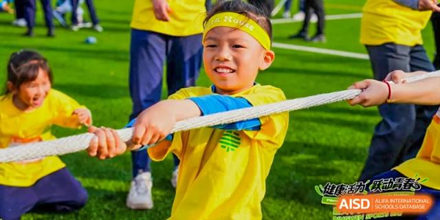 A young boy from Dingwen Academy Hangzhou in a yellow and blue shirt gripping a thick rope firmly during a tug-of-war competition.