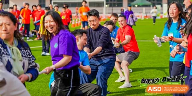 Adults and students from Dingwen Academy Hangzhou laughing while playing tug-of-war in a lively, casual match.