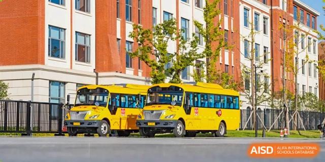 Two bright yellow school buses from Dingwen Academy Hangzhou parked outside the red-brick school building.