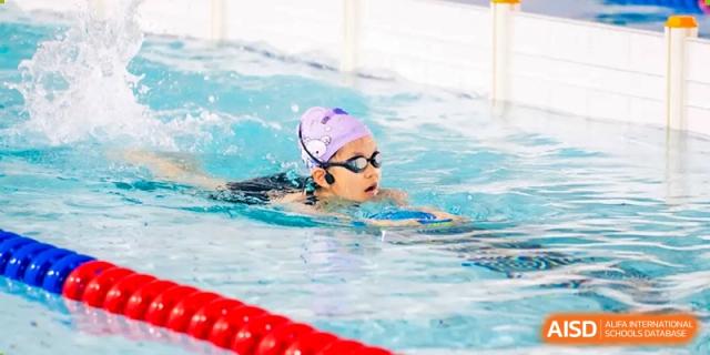 A student from Dingwen Academy Hangzhou swimming freestyle in a pool while wearing a purple swim cap and goggles.