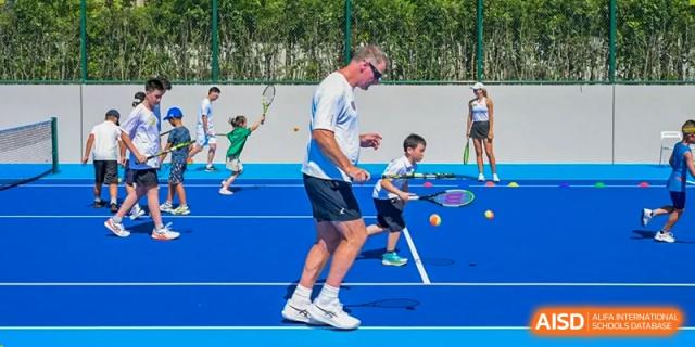 An instructor from Dingwen Academy Hangzhou teaching a young student how to play tennis on a bright blue court during a lesson.
