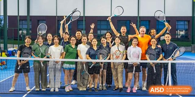 A large group of students and instructors from Dingwen Academy Hangzhou posing for a celebratory picture on a tennis court, holding rackets.