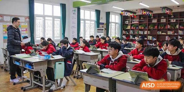 Students from Henan Zhengzhou Jianye International School seated at desks in a brightly lit classroom, focusing on their work or listening to a lesson.