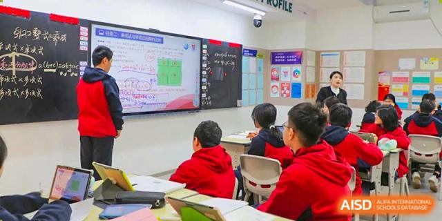Students from Henan Zhengzhou Jianye International School participating in a class with a digital display showing a graph and text on the wall.