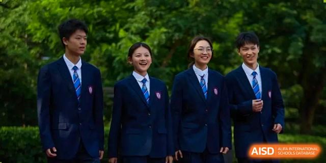 Two students from Henan Zhengzhou Jianye International School in uniform standing side-by-side, posing for a photo outdoors among trees.