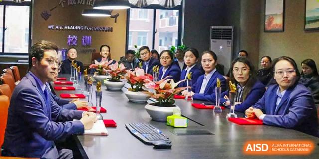 Female students from Henan Zhengzhou Jianye International School seated around a large table set with flowers, possibly during a cultural or tea ceremony event.