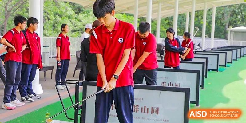 A student from Henan Zhengzhou Jianye International School in a red shirt concentrating on hitting a ball at a golf driving range during a sports lesson.