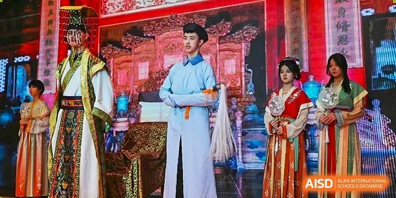 A student from Henan Zhengzhou Jianye International School dressed in a traditional Chinese costume standing on a brightly lit stage during a performance or ceremony.