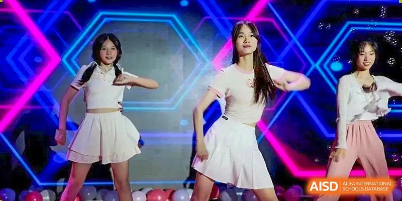 Students from Henan Zhengzhou Jianye International School performing a modern dance routine on stage, with one female student wearing a white skirt and top.
