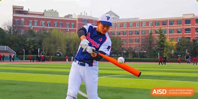 A male student from Henan Zhengzhou Jianye International School wearing a baseball uniform, swinging a baseball bat on an outdoor sports field.