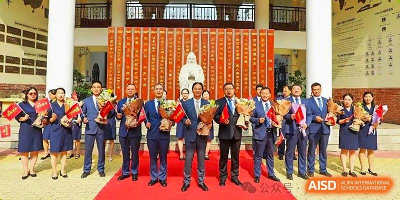 A group of teachers or staff members from Henan Zhengzhou Jianye International School posing with awards on a red carpet inside a school hall with a traditional statue.